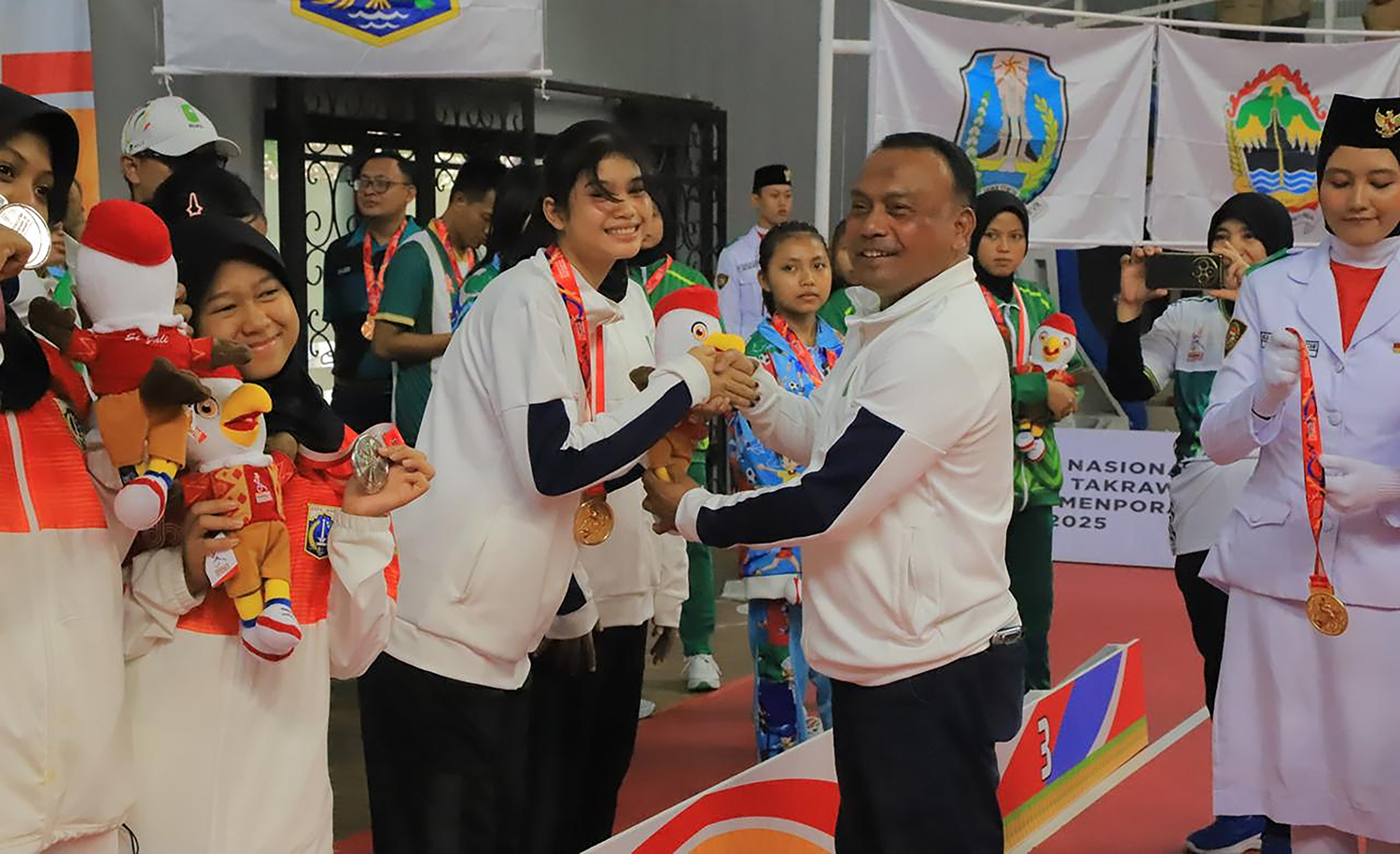 SERAHKAN MASKOT: Kadispora Riau Yurnalis menyerahkan maskot saat upacara penyerahan medali emas di GOR Cempaka Putih, Jakarta  Pusat, Rabu (5/11/2025).