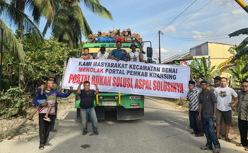 Sejumlah masyarakat Benai membawa spanduk menolak pemasangan portal di ruas jalan Simpang Mangga Kecamatan Benai, Jumat (7/11/2025).