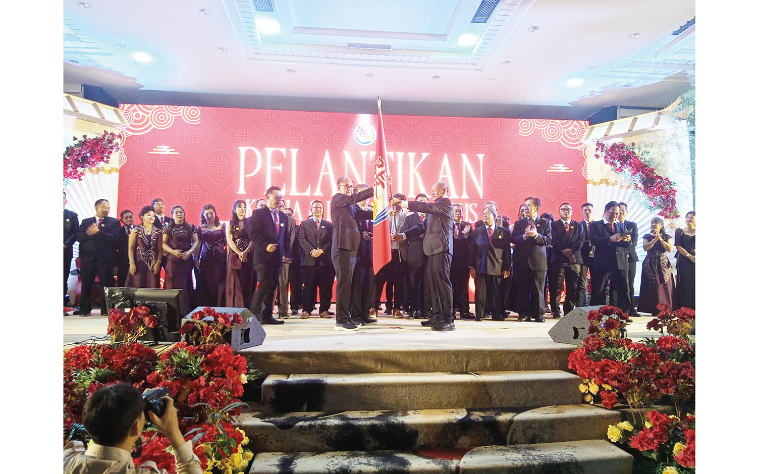 Dewan Pengawas Marga Zhang Riau, Pilemon Piterus (kiri), bersama Ketua Marga Zhang Riau Tio Po Kui (kanan) memegang bendera Persaudaraan Marga Zhang saat pelantikan di Hotel Furaya Pekanbaru, Sabtu (8/11/2025).