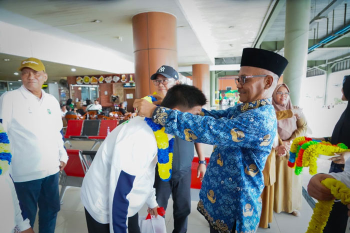Kepala SMANOR/SKO Riau Aslim SPd MPd mengalungkan bunga kepada atlet peraih medali Popnas XVII/2025 saat penyambutan kepulangan di Bandara SSK II Pekanbaru, Senin (10/11/2025).