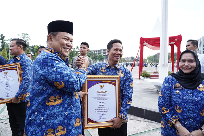 Plt Gubri, SF Hariyanto menyerahkan penghargaan UHC kepada Wabup H Muklisin dalam peringatan Hari Kesehatan Nasional, Senin (17/11/2025) di halaman Kantor Gubernur Riau.