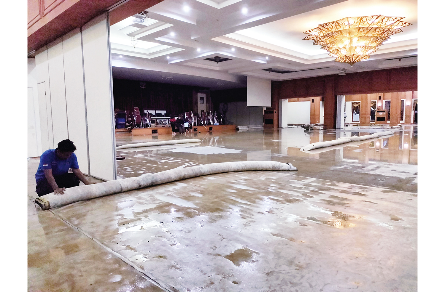 Petugas Satpol PP dan Damkar, BPBD dan MAS Tahfiz Rohul membersihkan dan menggulung karpet yang telah terendam genangan air di ruang Convention Hall Islamic Center Pasirpengaraian, Ahad (16/11/2025) malam.