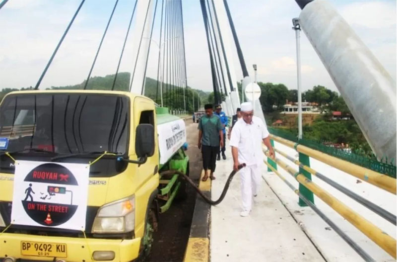 Ustaz Muhammad Candra P Pusponegoro Rizqi Marzaqah Al Hana (kanan, mengenakan pakaian serba putih) berjalan di samping truk tangki kuning berstiker Ruqyah On The Street.