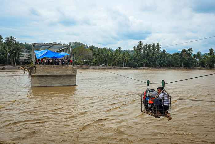 Warga desa meng&shy;gunakan kereta gantung darurat untuk menyeberangi sungai setelah jembatan hancur akibat banjir bandang di Bireuen, Aceh, Selasa (2/12/2025).