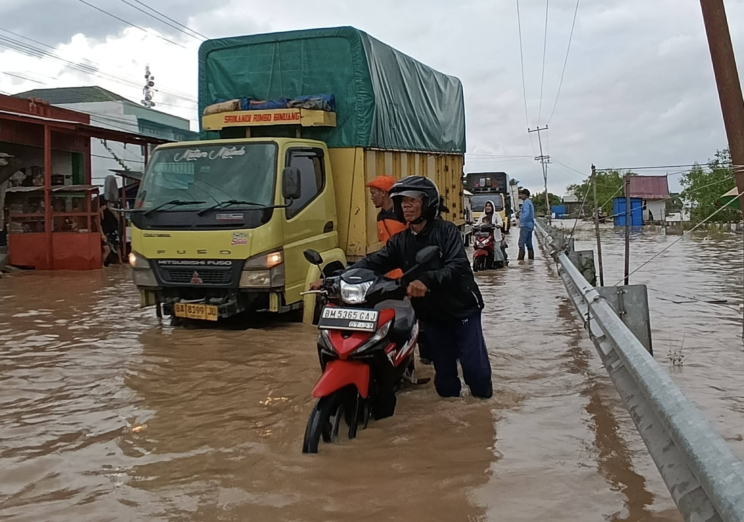 Masyarakat menuntun sepeda motor akibat mesin mati terendam air saat melintasi jalan Griliya, Parit 6, Tembilahan Hulu, Inhil, Sabtu (6/12/2025).