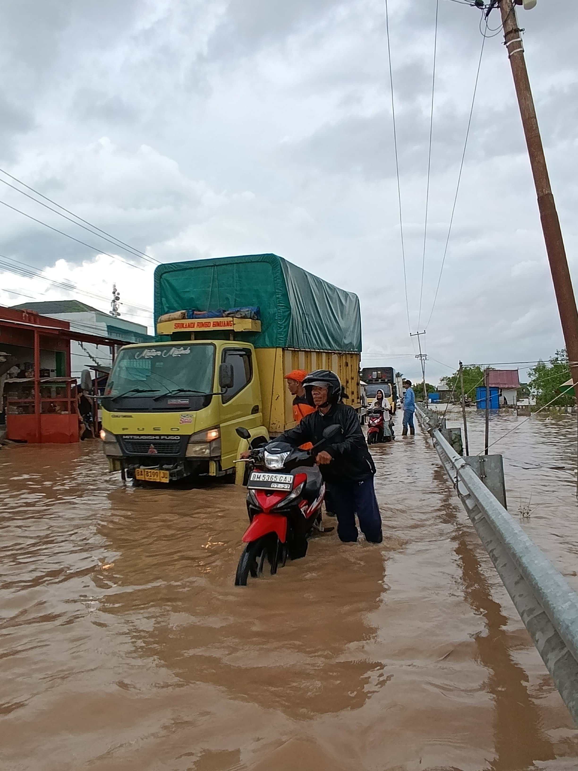 Seorang pengendara menuntun sepeda motor karena mesin mati akibat terendam air saat melintasi Jalan Gerilya, Parit 6, Tembilahan Hulu, Inhil, Sabtu (6/12/2025).
