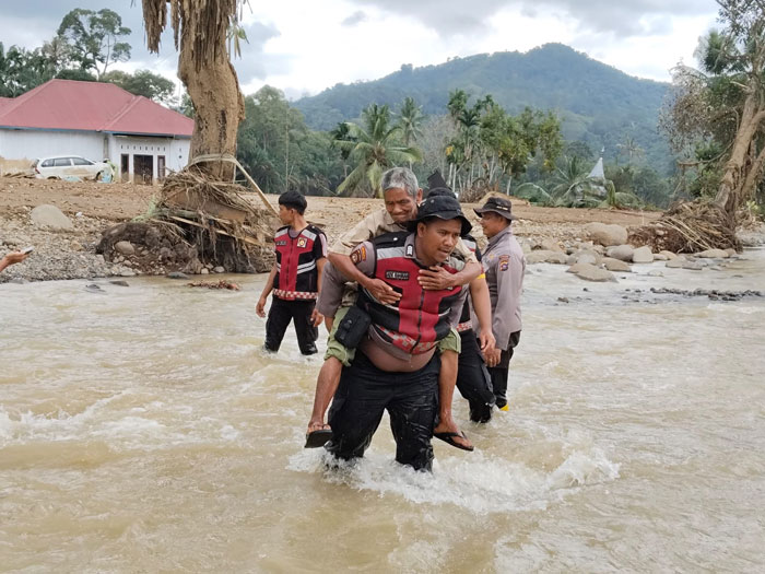 Personel Samapta Polda Riau membopong salah seorang warga Palembayan yang hendak menyeberangi sungai, Ahad (7/12/2025).
