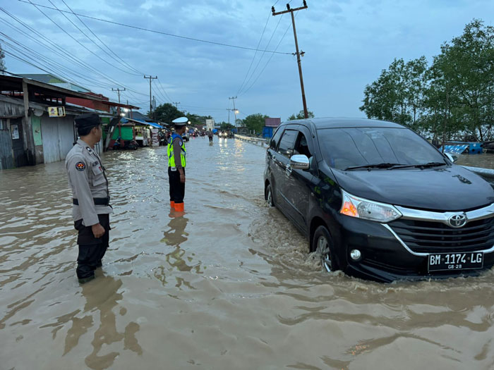 Petugas Kepolisian sedang mengatur lalu lintas di jalan yang tergenang air pasang di Jalan Lintas Tembilahan-Rengat tepatnya di Parit 6, Kecamatan Tembilahan Hulu
