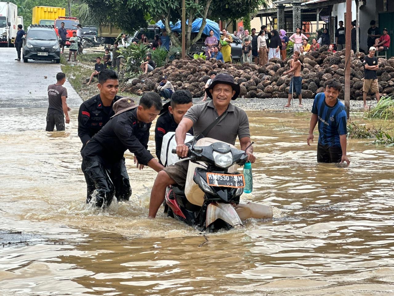 Petugas dari Satbrimob Polda Riau Batalyon C Pelopor turut membantu pemotor saat melintasi Jalan Lintas Timur akibat luapan Sungai Akar, di wilayah Kabupaten Inhu, Ahad (14/12/2025).