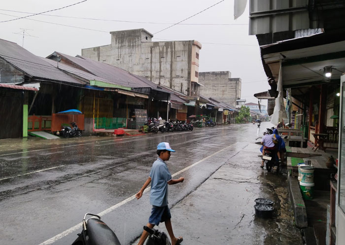 Hujan melanda Bagansiapiapi, sejumlah penguna jalan memilih berteduh di emperan rumah warga, Senin (15/12/2025).