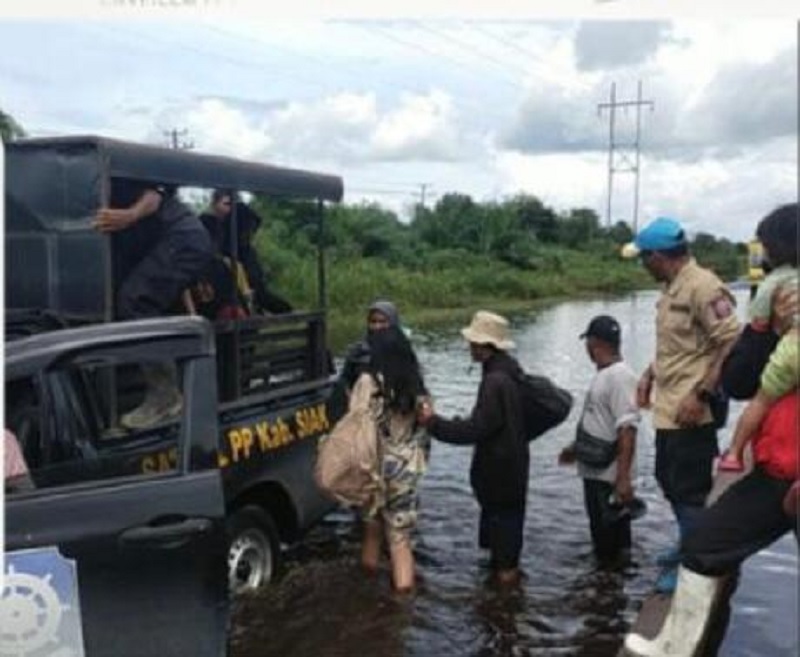 Warga dibantu menaiki mobil Satpol PP untuk melintasi Jalan Nasional Siak-Tanjung Buton, Km 29, Simpang Obor, Kampung Dosan, Kecamatan Pusako, Kabupaten Siak, Sabtu (20/12/2025).