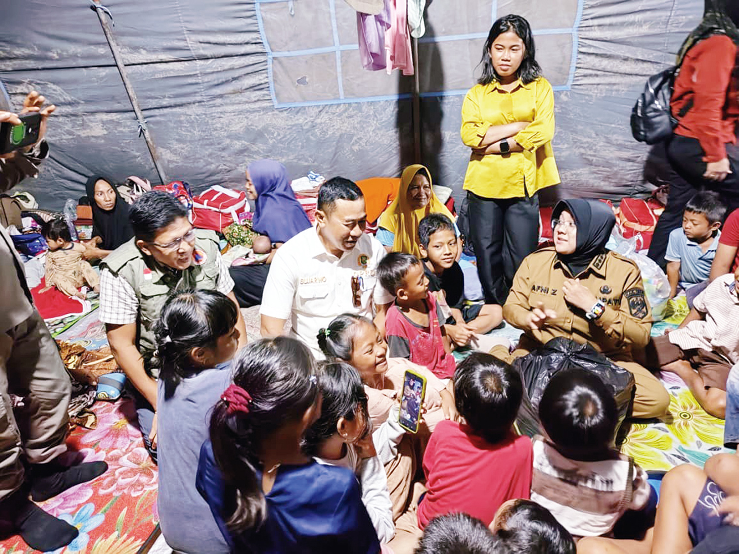 Bupati Siak Afni Z bersama Ketua Komisi II DPRD Siak Sujarwo bercengkerama dengan anak-anak warga Kampung Dosan di tenda pengungsian Kampung Sungai Limau, Kecamatan Pusako, Kabupaten Siak, Senin (22/12/2025).