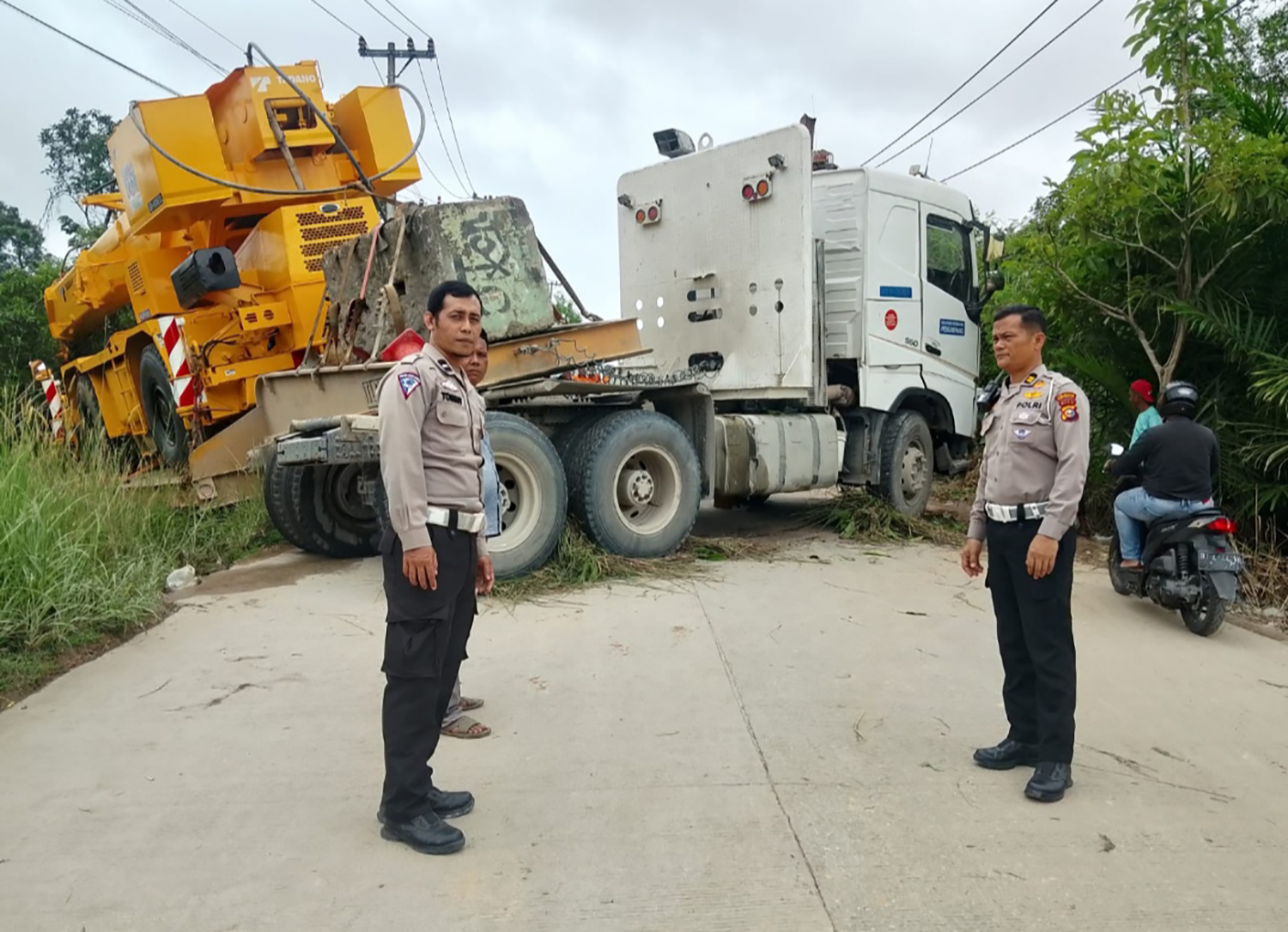 Petugas kepolisian berada di lokasi truk trailer bermuatan crane yang gagal menanjak dan melintang di Jalan Badak, Kecamatan Tenayan Raya, Selasa (30/12/2025).