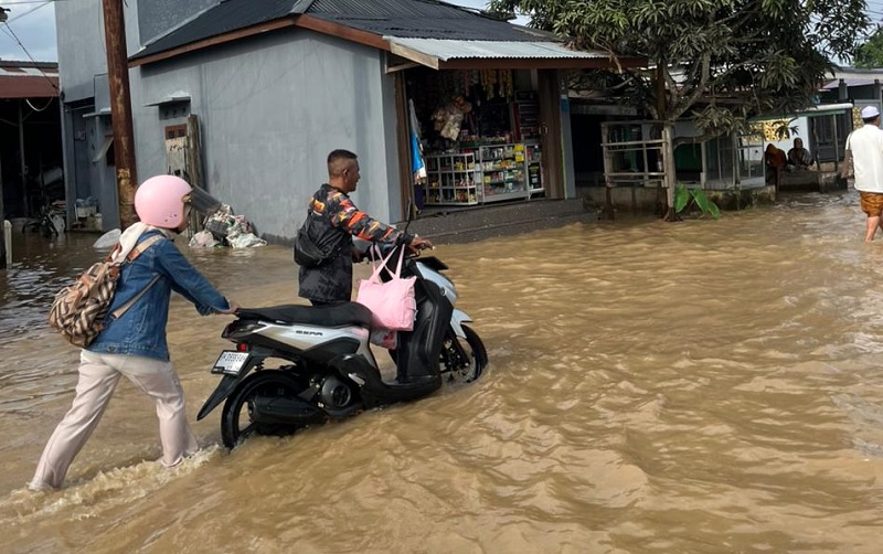 Petugas BPBD Inhil membantu mendorong sepeda motor pengendara yang mogok setelah melintasi jalan yang terendam air pasang di Tembilahan, Ahad (4/1/2026).