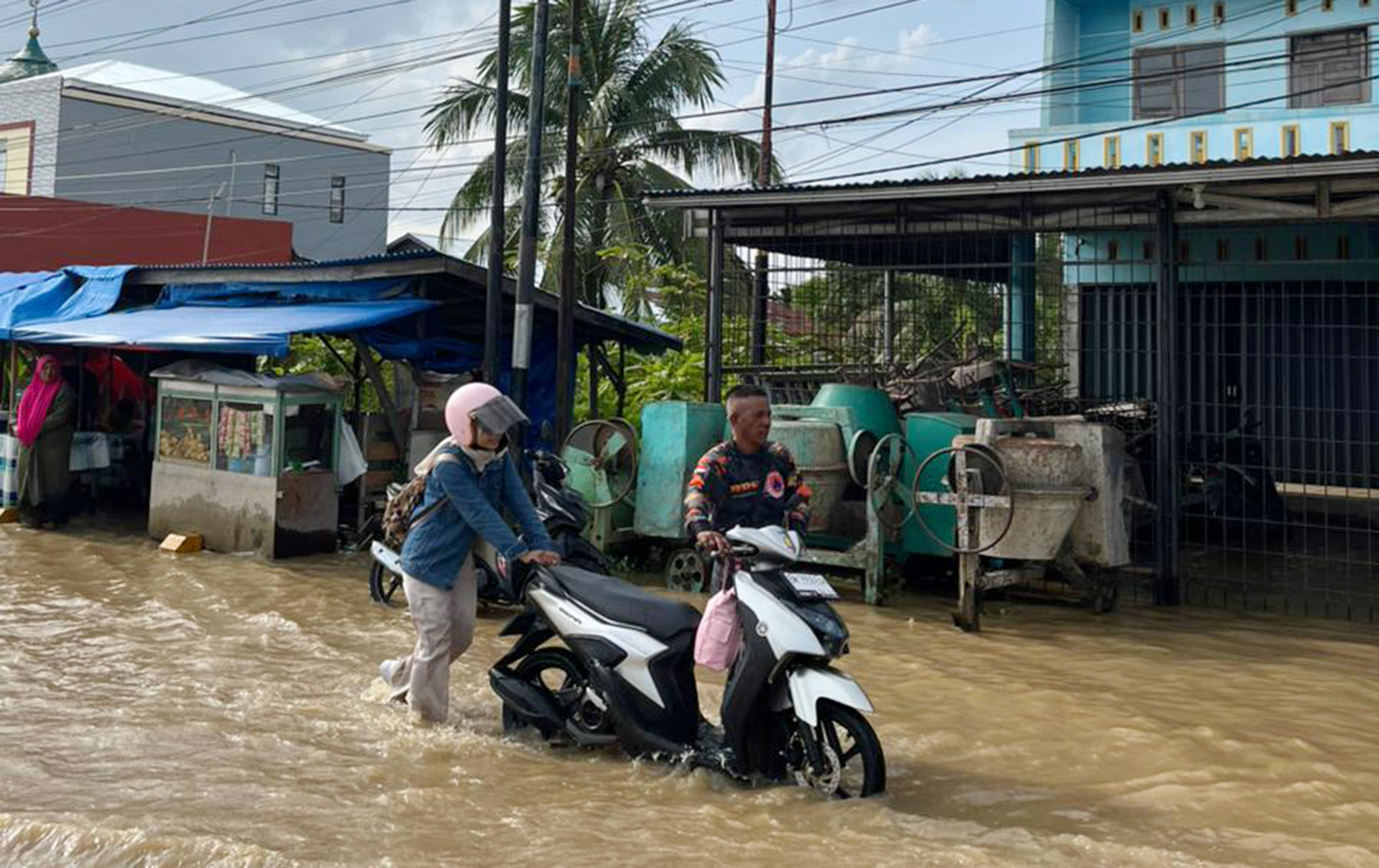 Petugas BPBD membantu mendorong sepeda motor pengendara yang mogok setelah melintasi jalan yang terendam air pasang di Tembilahan, Indragiri Hilir, Ahad (4/1/2026).