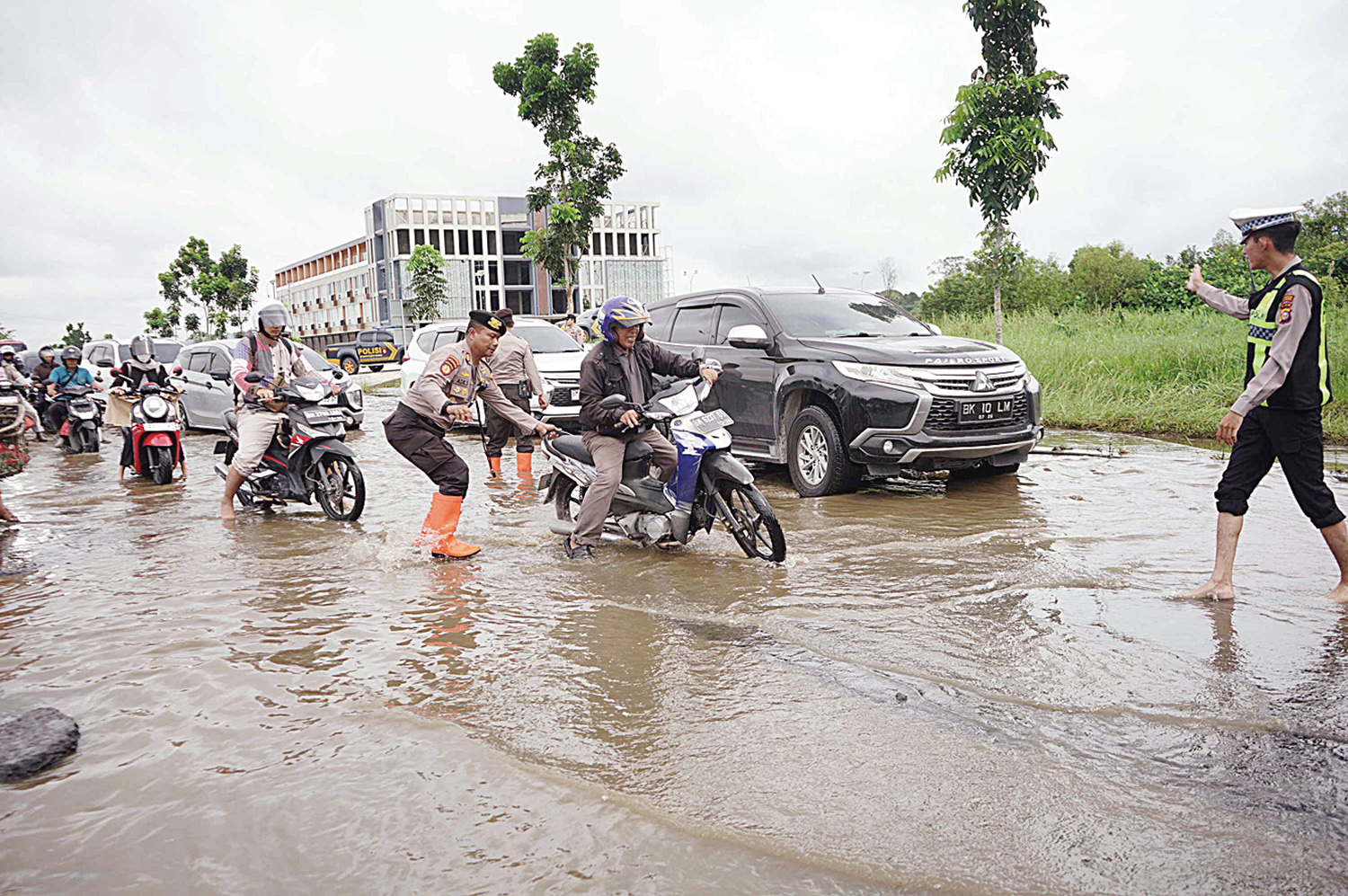 Petugas kepolisian membantu pengendara yang berusaha melewati banjir yang menggenangi Jalan Sudirman Pekanbaru, Rabu (7/1/2026).