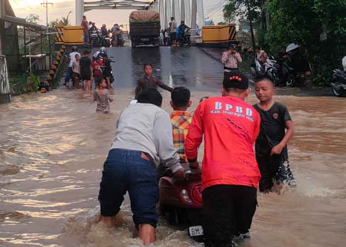 Personel Badan Penanggulangan Bencana Daerah Indragiri Hilir membantu warga mendorong sepeda motor mogok setelah melewati jalan yang digenangi banjir di Tembilahan, Kamis (8/1/2026).