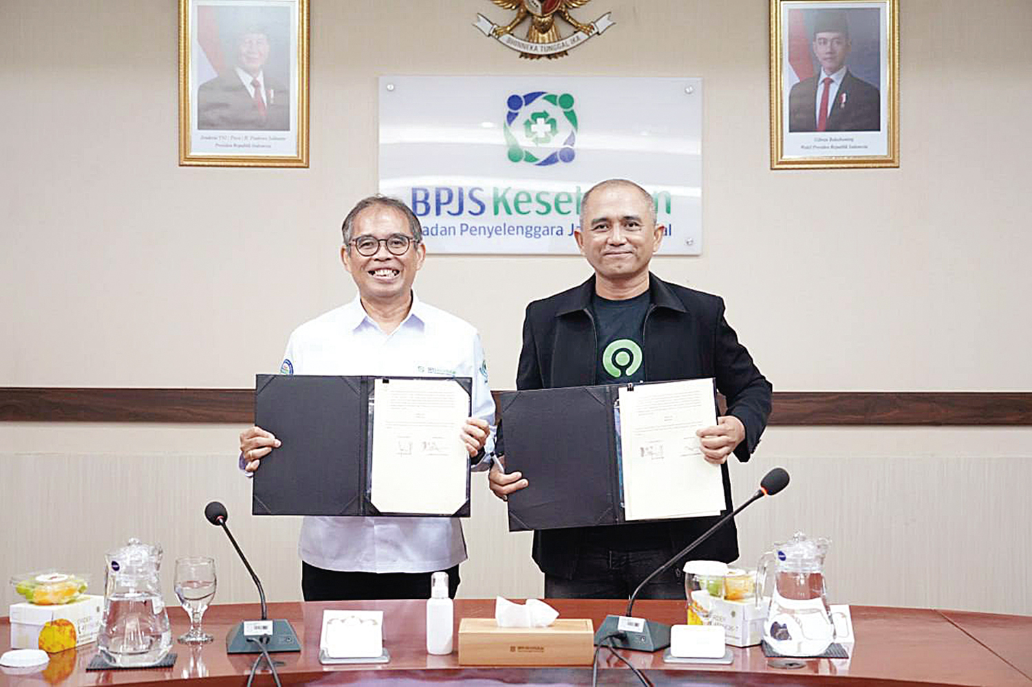 Direktur Kepesertaan BPJS Kesehatan David Bangun (kiri) bersama Direktur Operasional Gojek Bambang Adi Wirawan (kanan) menunjukkan naskah perjanjian kerja sama antara BPJS Kesehatan dan PT GoTo Gojek.