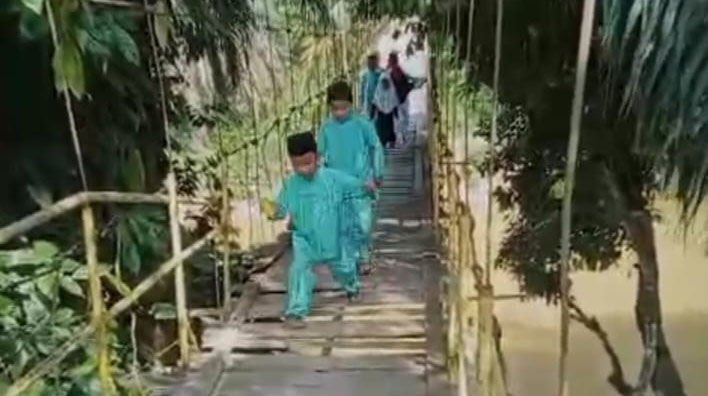 Anak-anak sekolah melintasi jembatan gantung Desa Muara Tiu Kecamatan Pucuk Rantau.
