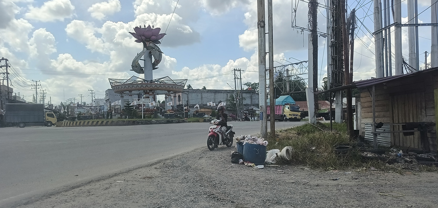 Seorang pengendara sepeda motor menutup hidung saat melewati tumpukan sampah di Jalan Pematang Reba, persisnya di Simpang Empat Tugu Ikan Patin, Kecamatan Rengat Barat, Rabu (11/2/2026).