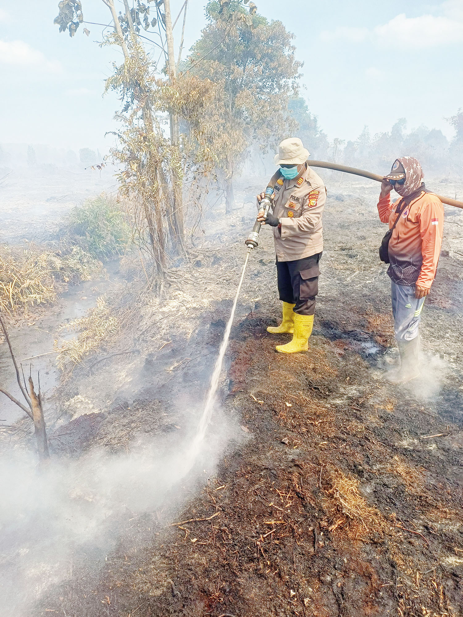 Kapolsek Rupat AKP Faisal bersama personel BPBD Bengkalis menyemprotkan air saat melakukan pendinginan lahan yang terbakar di Jalan Parit Jawa RT 004 RW 002 Du