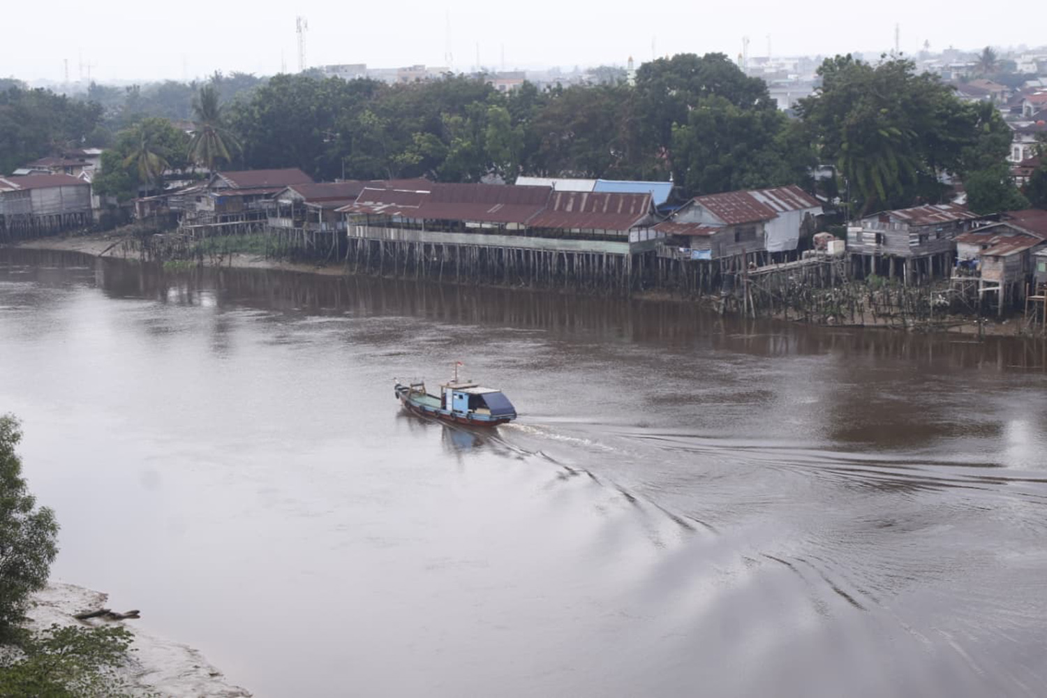 Sebuah perahu melintasi Sungai Siak yang di pinggirnya terdapat permukiman penduduk. Foto diambil beberapa waktu lalu. 