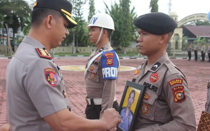 Kapolres Bengkalis AKBP Fahrian Saleh Siregar sedang menyilang foto Aipda Asmadi yang secara resmi di PTDH di Mako Polres Bengkalis, Senin (2/3/2026).