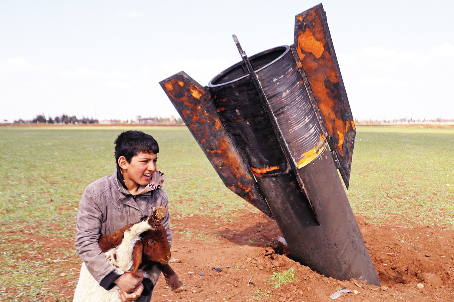 Seorang anak laki-laki bermain dengan dombanya di samping rudal yang belum meledak di pinggiran Qamishli, Suriah Timur, Kamis (5/3/2026). 