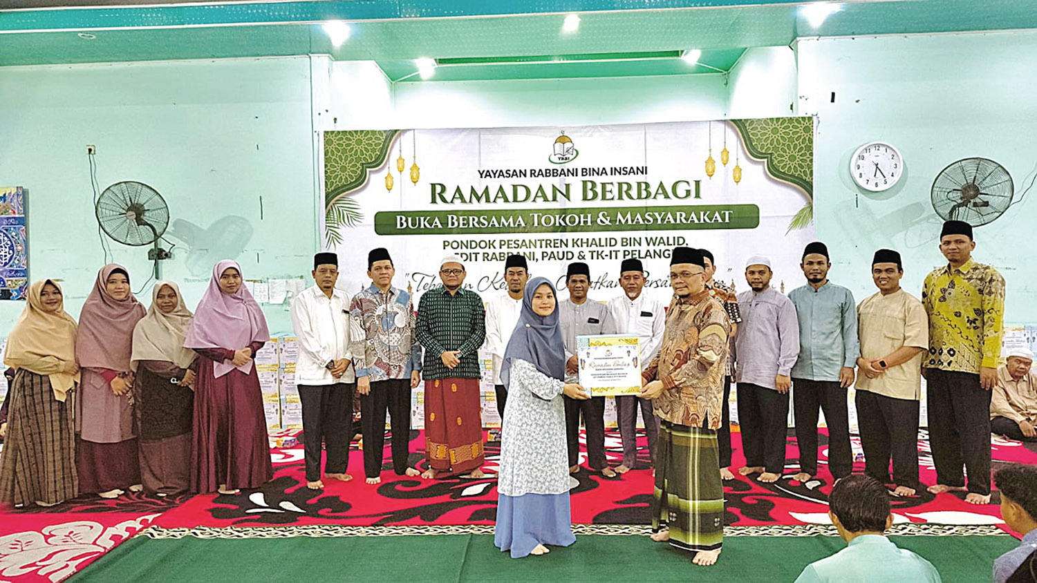 Penyerahan paket sembako secara simbolis dari Ketua YRBI H Roudhatul Firdaus LC MPd kepada Ketua Panitia Pelaksana Kegiatan Hj Elga Maharani LC, Ah