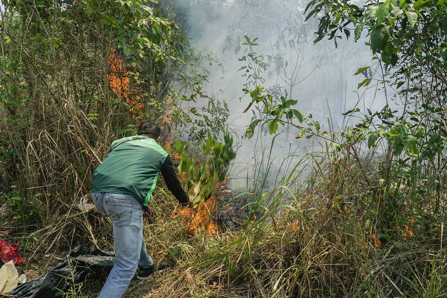 Seorang Driver Ojol melakukan upaya pemaadaman Lahan kosong dengan vegetasi mineral yang terbakar di Jalan Rajawali Sakti, Pekanbaru, Selasa (10/3/2026) ft: MHD AKHWAN/RIAUPOS