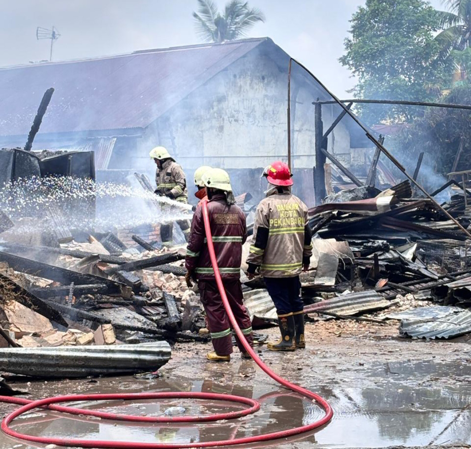 Petugas Pemadam Kebakaran Kota Pekanbaru menyemprotkan air ke puing-puing bangunan yang terbakar di Jalan Pepaya ujung, Kecamatan Sukajadi, Senin (30/3/2026) siang. 