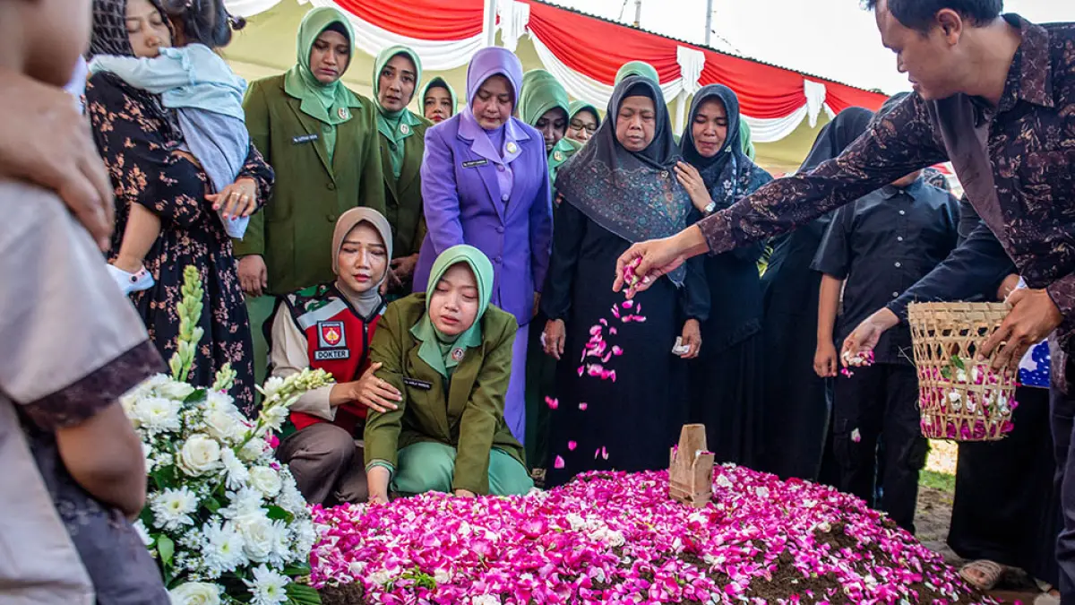 Fafa Nur Azila (berlutut kedua dari kiri) menangis di atas makam suaminya Farizal Rhomadhon saat anggota keluarga menaburkan bunga selama pemakaman di Taman Makam Pahlawan Giripeni di Kulon Progo, Yogyakarta, Ahad (5/4/2026). (DEVI RAHMAN/AFP)