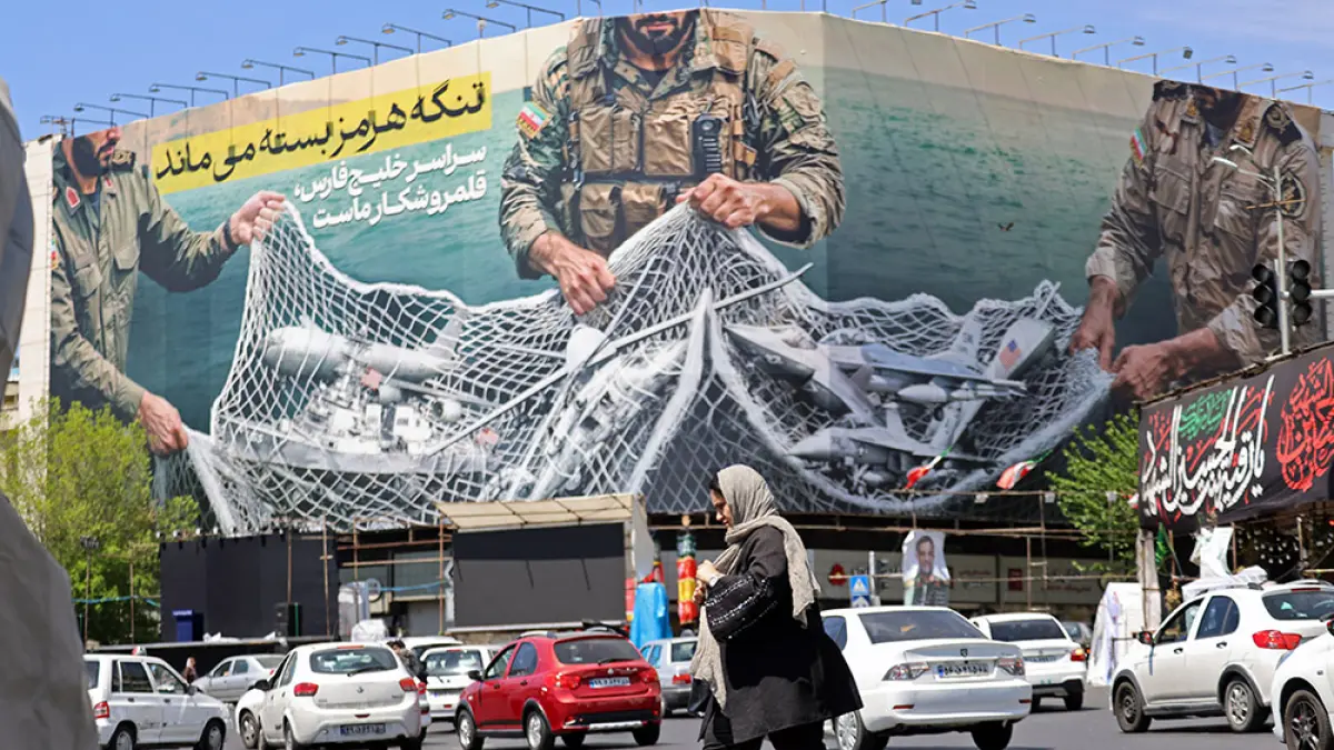 MELEWATI REKLAME RAKSASA: Seorang wanita berjalan melewati papan reklame raksasa bertuliskan ‘Selat Hormuz Tetap Ditutup’ di Lapangan Revolusi, Teheran, Ahad (12/4/2026). Ketua parlemen Iran Mohammad Bagher Ghalibaf yang ikut dalam pembicaraan perdamaian dengan Amerika Serikat mengatakan Washington “tidak mampu” memenangkan kepercayaan Teheran selama diskusi tersebut. (ATTA KENARE/AFP)