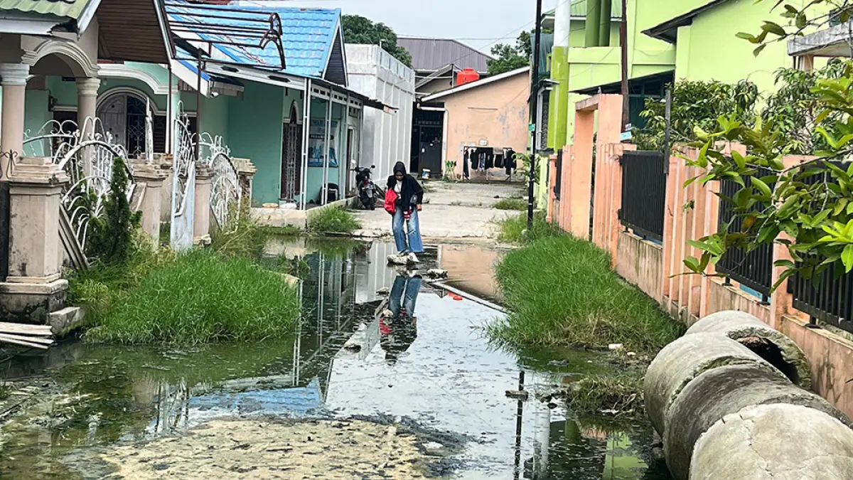 Seorang  warga kesulitan melintas di ruas Jalan Merpati, Kecamatan Binawidya yang tergenang air yang sudah menghitam, Kamis (7/5/2026). (Prapti Dwi Lestari/riau pos)