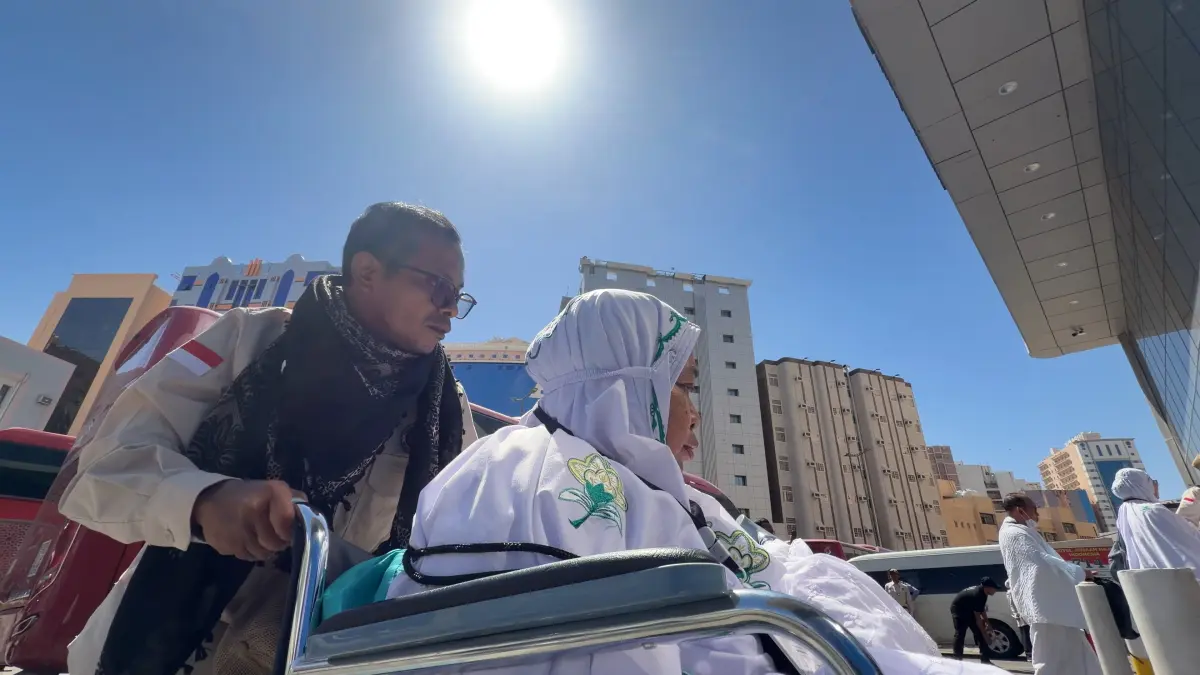 Petugas membantu mendorong jemaah calon haji lanjut usia yang memakai kursi roda di tengah cuaca panas Makkah, Sabtu (16/5/2026). https://haji.go.id