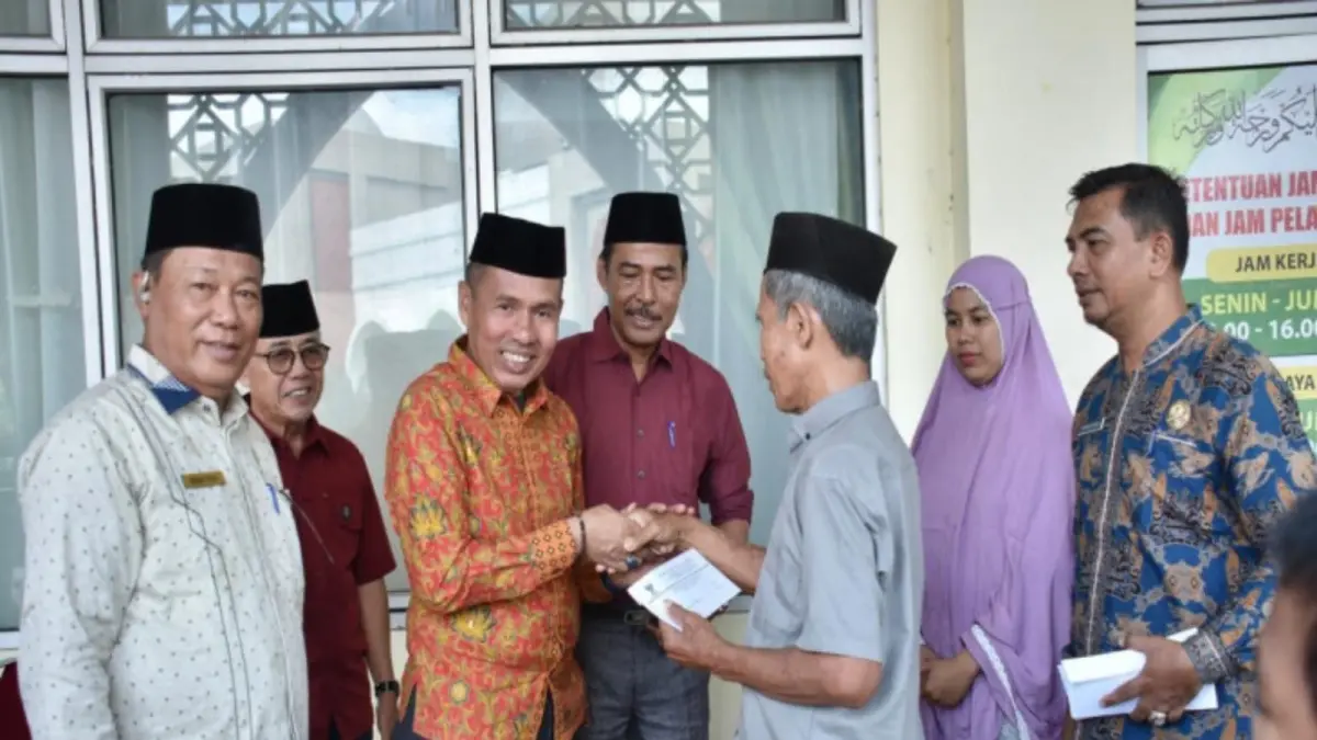 Ketua Baznas Kampar Arizon menyerahkan bantuan secara simbolis kepada para penerima manfaat, Kamis (25/6/2026).(DISKOMINFO KAMPAR UNTUK RIAUPOS.CO)