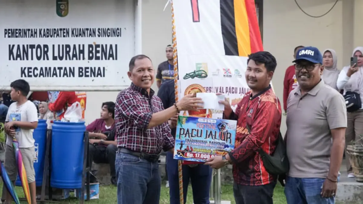 Asisten III Setda Kuansing Drs Azhar MM menyerahkan hadiah Juara I pada perwakilan  Jalur Kahulu Jantan Danau Kompe Desa Benai Kecil usai perpacuan disaksikan Camat Benai, Paimun Hendro, Ahad (12/7/2026). (Desriandi Candra/Riaupos.co)