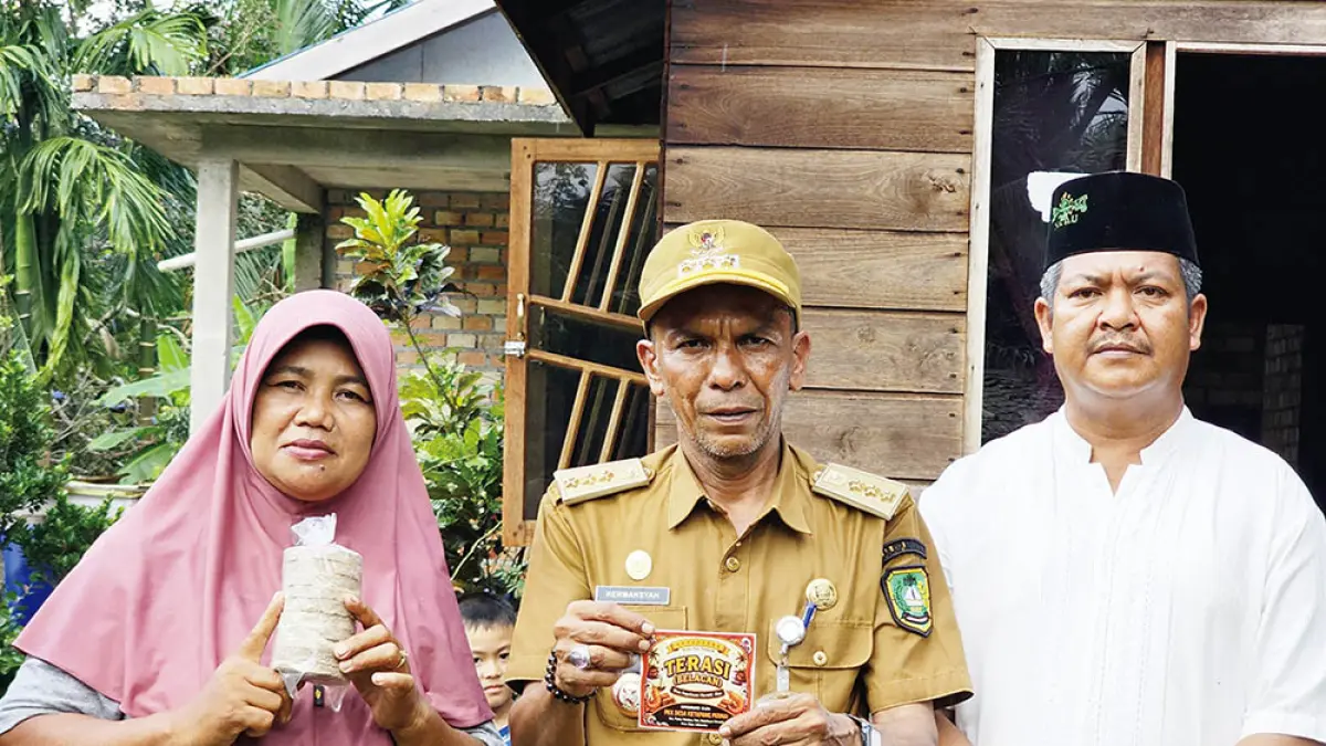 Suryati pelaku usaha terasi bersama Kepala Desa Ketapang Permai, Safrizal, dan Camat Pulau Merbau, Hermansyah memperlihatkan produk hasil usaha, Ahad (12/7/2026).(WIRA SAPUTRA/RIAU POS)