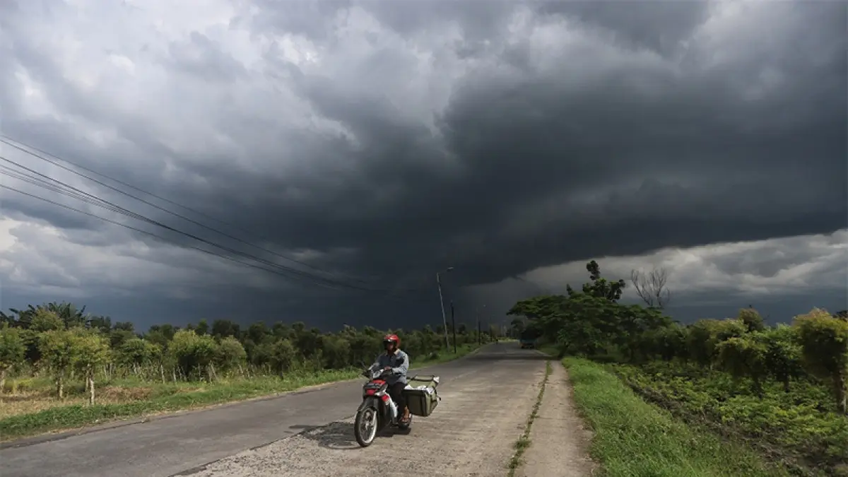 Ilustrasi cuaca ekstrem, mendung hitam terlihat di atas pengendara motor. (Dok Jawapos.com)