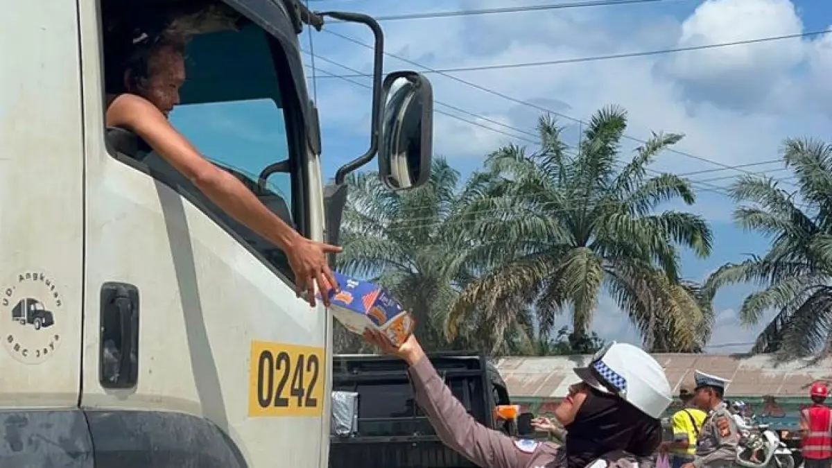 Personel Satlantas Polres Pelalawan memberikan bantuan makanan dan minuman kepada para pengemudi kendaraan yang terjebak antrean di Jalintim KM 75, Jumat (17/7/2026). (Amin/Riaupos.co)