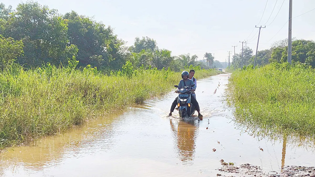 TERGENANG: Pengendara sepeda motor kesulitan saat melintas di Jalan Fajar Raya, Kecamatan Payung Sekaki yang tergenang, Selasa (21/7/2026). Jalan ini merupakan akses satu-satunya menuju ke SMAN 17 Pekanbaru dan masih berupa jalan tanah. (EVAN GUNANZAR/RIAU POS)