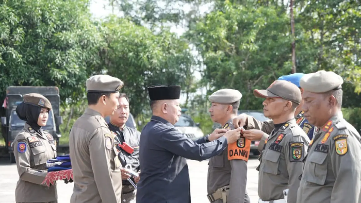 Pj Sekda Kuansing Drs Muradi MSi memasangkan pita secara simbolis pada personel Satpol PP-PKP Kuansing yang menjadi pasukan pengamanan even pacu jalur di tepian Narosa Teluk Kuantan, Selasa (4/8/2026) di halaman Satpol PP Kuansing. (Istimewa)