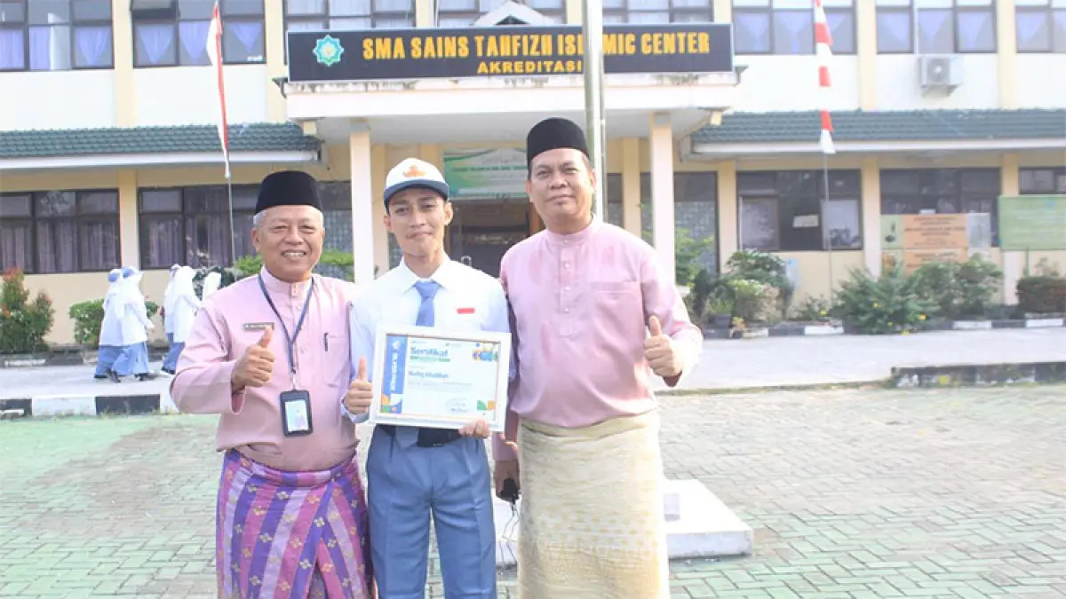 Kepala SMA Sains Tahfizh Islamic Center Siak Drs H Nursya foto bersama Afiq dan Wakil Kepala Sekolah Bidang Kesiswaan Frenki Putra Farma SPd di depan sekolah, Kamis (6/8/2026). (Istimewa)