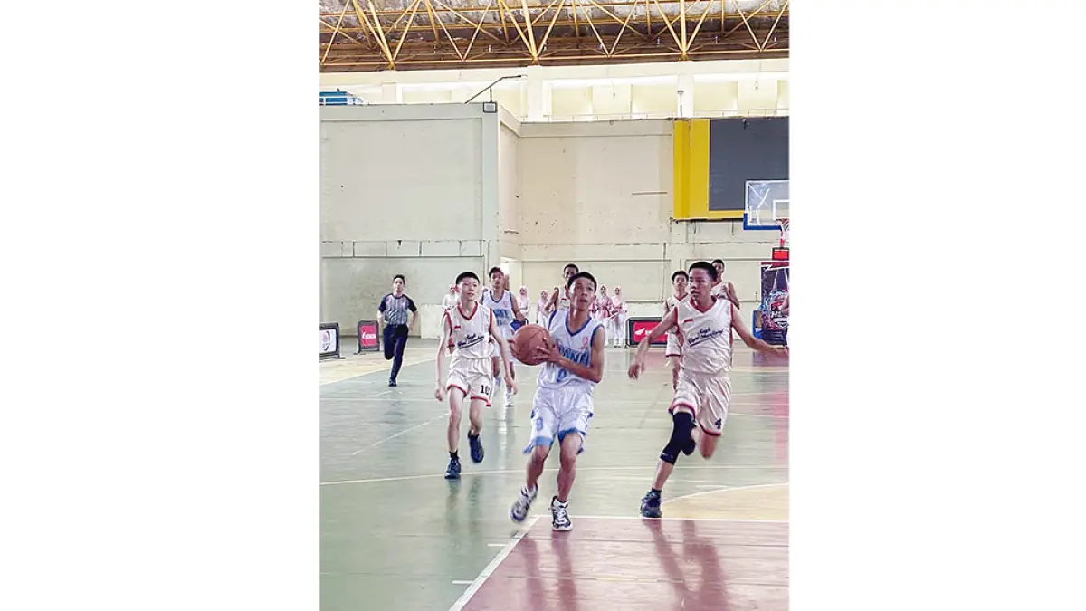 Pemain basket SMAN 5 Tualang (putih) membawa bola dan coba diadang pemain basket dari  SMKS YPPI (krem) pada pertandingan Riau Pos-HSBL Perawang Series 2026 di GOR Tualang, Kamis (6/8/2026).(monang lubis/riau pos)