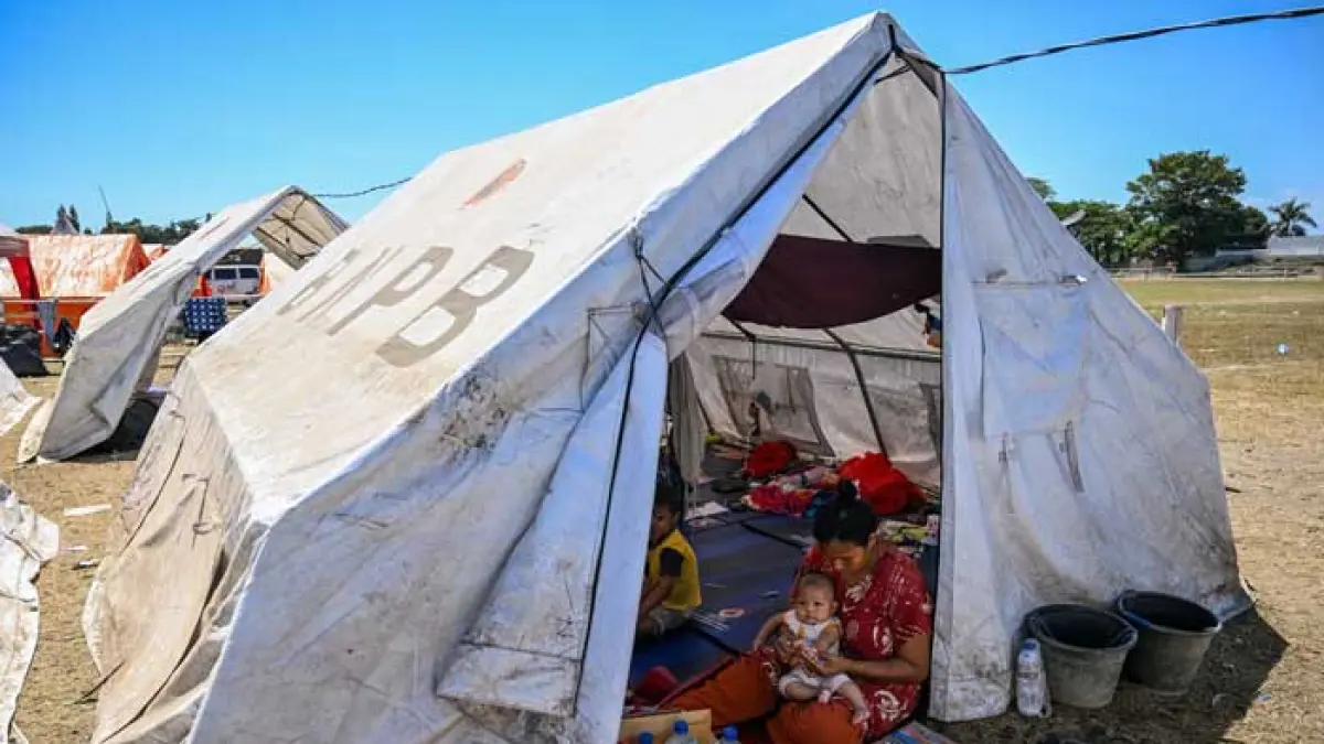 Seorang korban gempa menggendong anak saat duduk dalam tenda pengungsian di Maumere, Nusa Tenggara Timur, Selasa (18/8/2026). JUNI KRISWANTO / AFP