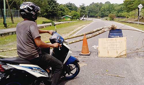 DITUTUP: Seorang warga melintas di kawasan Universitas Riau, di mana jalan dari Gerbang Arengka II ditutup sampai batas waktu tidak ditentukan, Senin (17/9/2018). (SAKIMAN/RIAU POS)