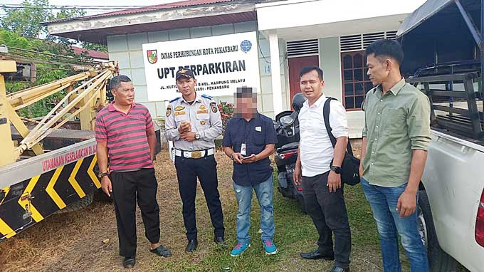 Oknum jukir (tengah) saat diserahkan petugas Polsek Bukit Raya ke Kantor UPT Perparkiran Dishub Pekanbaru, Senin (12/6/2023).
