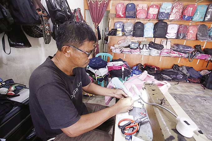 Pemilik usaha perbaikan tas memperbaiki tas di tokonya di Jalan Rajawali Sakti, Kecamatan Binawidya, Senin (3/7/2023). Jelang memasuki tahun ajaran baru, permintaan perbaikan tas sekolah mengalami peningkatan hingga 50 persen.