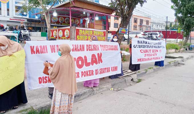 Ibu-ibu dari Kelurahan Tobek Godang membentang spanduk bertulisan warna merah saat menggelar aksi protes kehadiran Joker Poker Pub dan KTV di pinggir Jalan HR Soebrantas, Kecamatan Bina Widya, Kamis (15/12/2022).