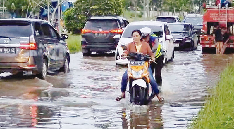Personel Satlantas Polres Pelalawan membantu pengendara sepeda motor yang mati mesin akibat menempuh Jalan Sultan Syarif Hasyim yang terendam banjir, Selasa (26/12/2023) siang.